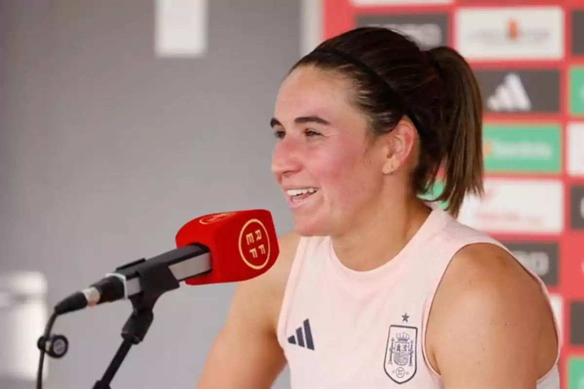 Futbolista sonriente con camiseta de la selección española dando una entrevista frente a un micrófono rojo Futbolista sonriente con camiseta de la selección española dando una entrevista frente a un micrófono rojo