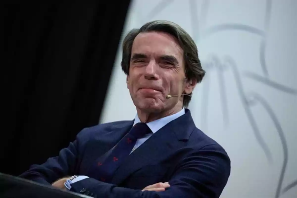 Hombre de mediana edad con cabello canoso y traje azul marino sonriendo mientras lleva un micrófono de diadema Hombre de mediana edad con cabello canoso y traje azul marino sonriendo mientras lleva un micrófono de diadema