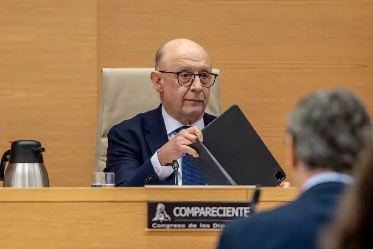 Hombre mayor con gafas y traje sosteniendo una tablet durante una comparecencia en una sala de reuniones del Congreso de los Diputados Hombre mayor con gafas y traje sosteniendo una tablet durante una comparecencia en una sala de reuniones del Congreso de los Diputados
