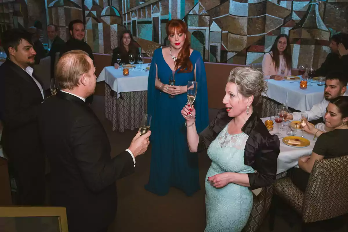 Personas elegantemente vestidas brindando con copas de champán en un restaurante mientras otros invitados observan y conversan en las mesas Personas elegantemente vestidas brindando con copas de champán en un restaurante mientras otros invitados observan y conversan en las mesas