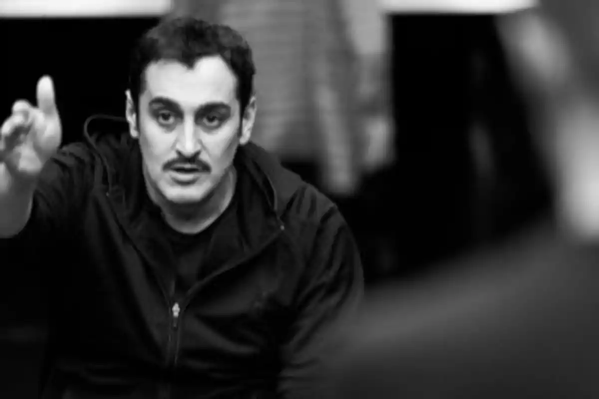 Hombre de cabello corto y bigote gesticulando con la mano extendida en una imagen en blanco y negro Hombre de cabello corto y bigote gesticulando con la mano extendida en una imagen en blanco y negro