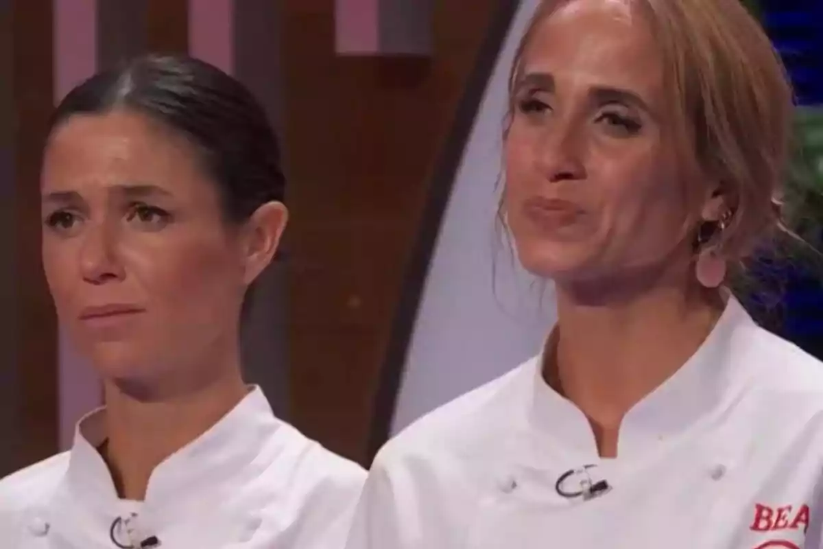 Gabriela y Bea con chaquetas de chef blancas muestran expresiones serias y emotivas en un set de competencia culinaria de MasterChef.