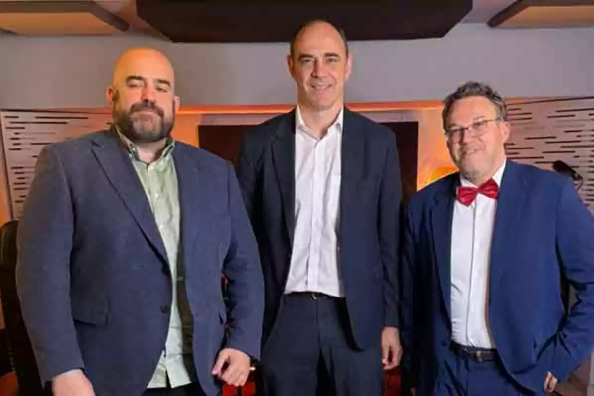 Tres hombres vestidos con traje posan juntos en un ambiente interior elegante