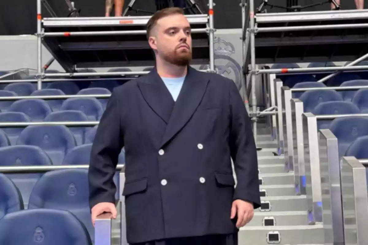 Hombre con barba y saco azul posando en unas gradas de estadio Hombre con barba y saco azul posando en unas gradas de estadio