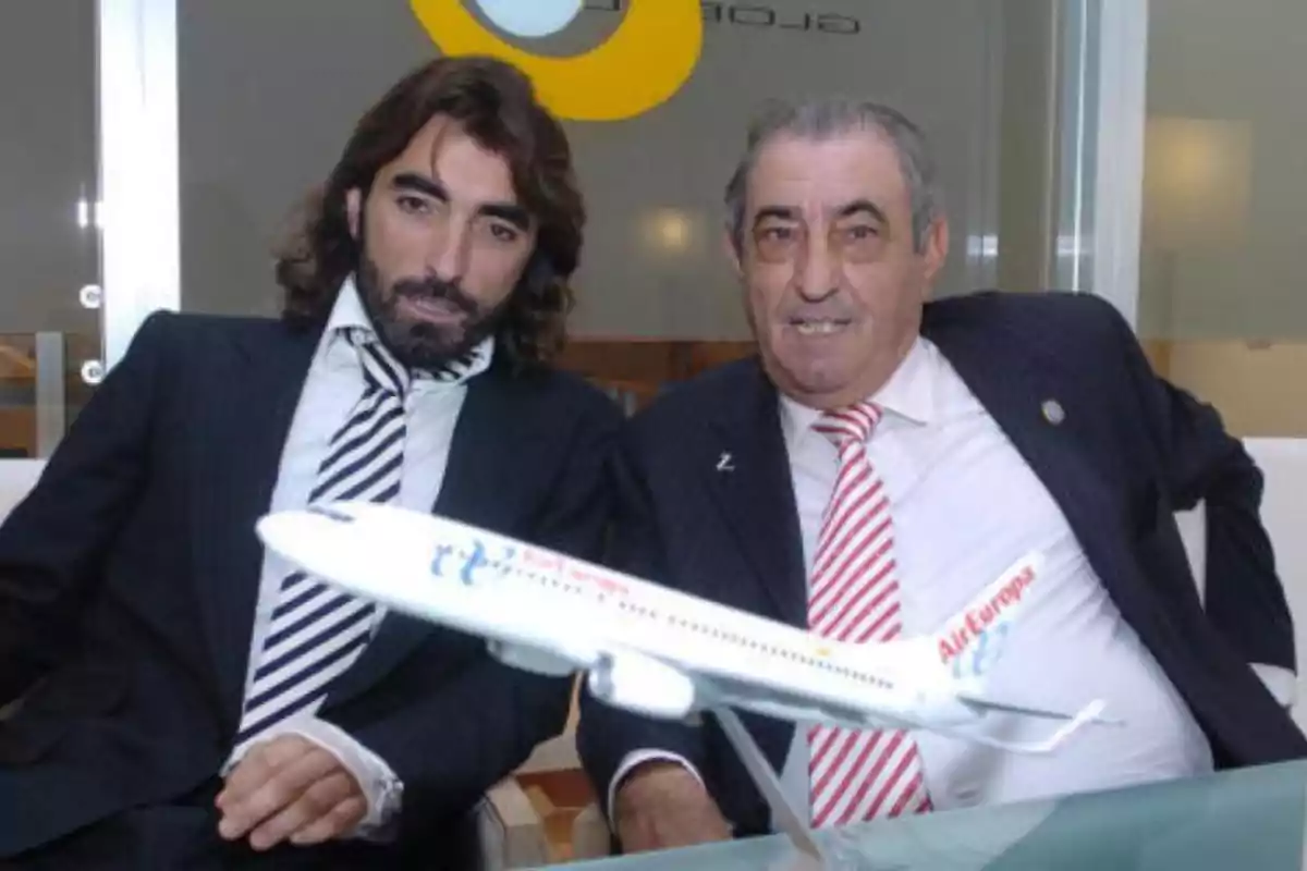 Dos hombres con traje y corbata posan sentados junto a una maqueta de un avión de Air Europa sobre una mesa.