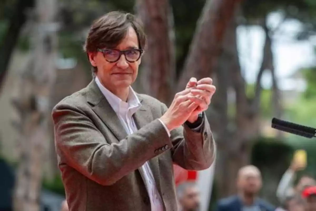 Hombre con gafas y chaqueta marrón aplaudiendo al aire libre con árboles de fondo Hombre con gafas y chaqueta marrón aplaudiendo al aire libre con árboles de fondo