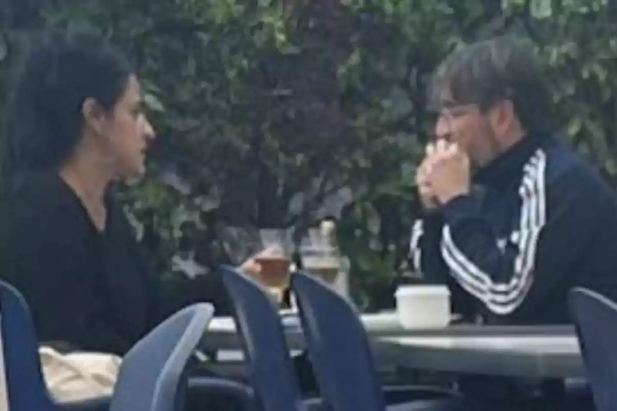 Dos personas sentadas en una mesa al aire libre conversando mientras toman bebidas Dos personas sentadas en una mesa al aire libre conversando mientras toman bebidas