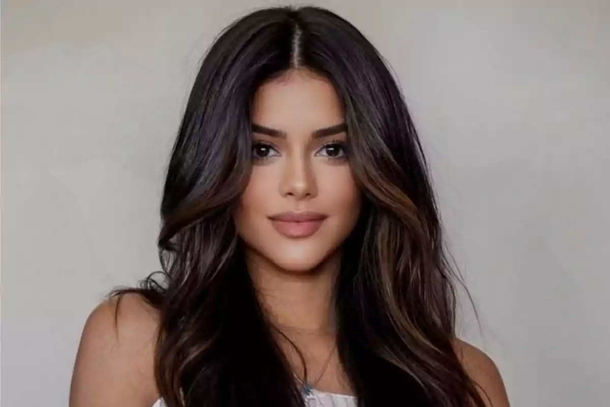 Mujer joven de cabello largo y oscuro con ondas suaves y maquillaje natural posando frente a un fondo claro