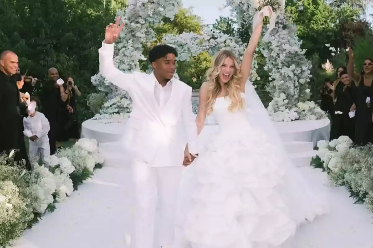 Pareja de recién casados caminando felices por el pasillo decorado con flores blancas en una boda al aire libre mientras los invitados celebran