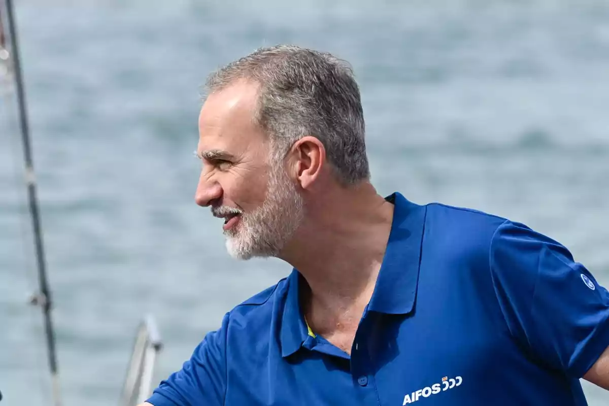 Hombre de cabello canoso y barba con camiseta azul sonríe mientras está en un barco frente al mar Hombre de cabello canoso y barba con camiseta azul sonríe mientras está en un barco frente al mar
