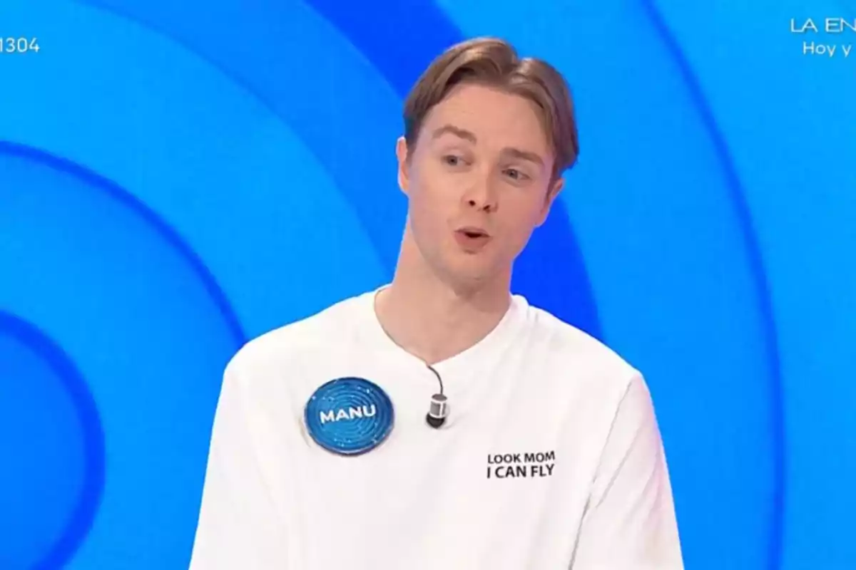 Manu con camiseta blanca y micrófono participando en un programa de televisión con fondo azul Manu con camiseta blanca y micrófono participando en un programa de televisión con fondo azul