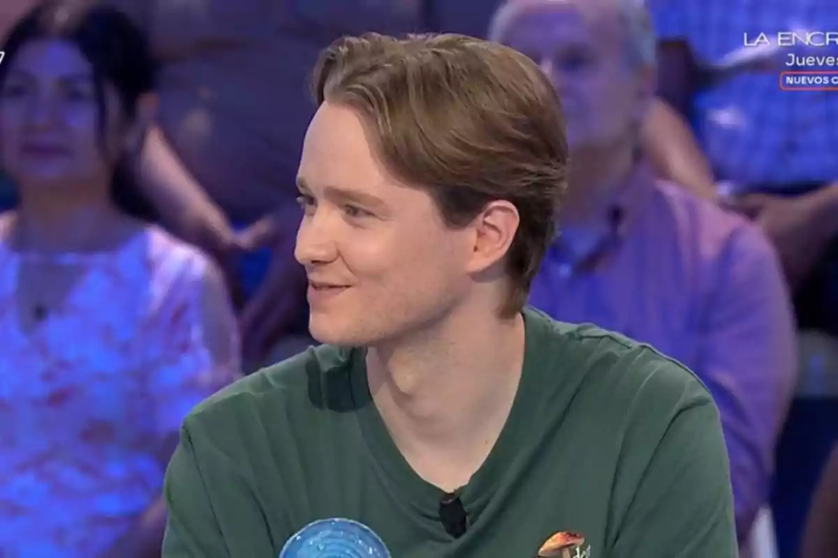 Manu de cabello castaño claro y camiseta verde sentado en un programa de televisión con público al fondo Manu de cabello castaño claro y camiseta verde sentado en un programa de televisión con público al fondo