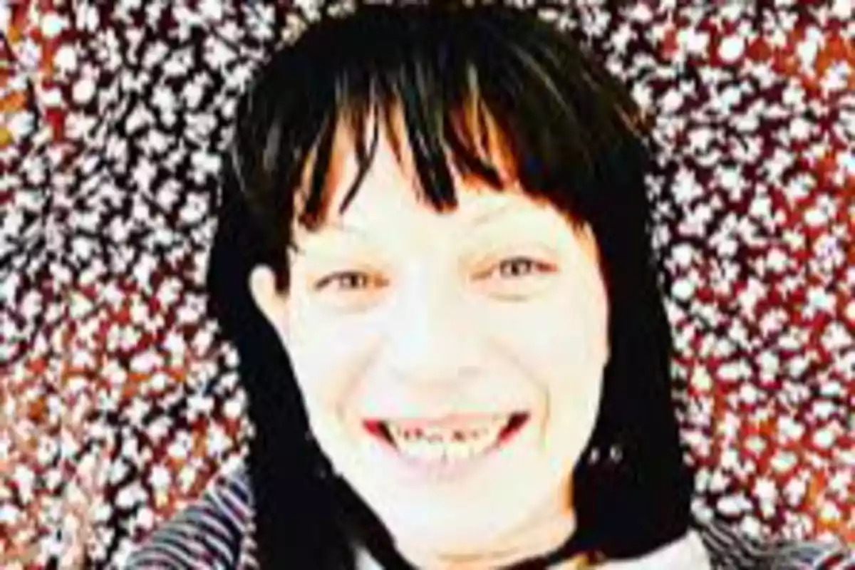 Persona sonriendo con cabello oscuro y flequillo sobre un fondo de flores blancas y rojas