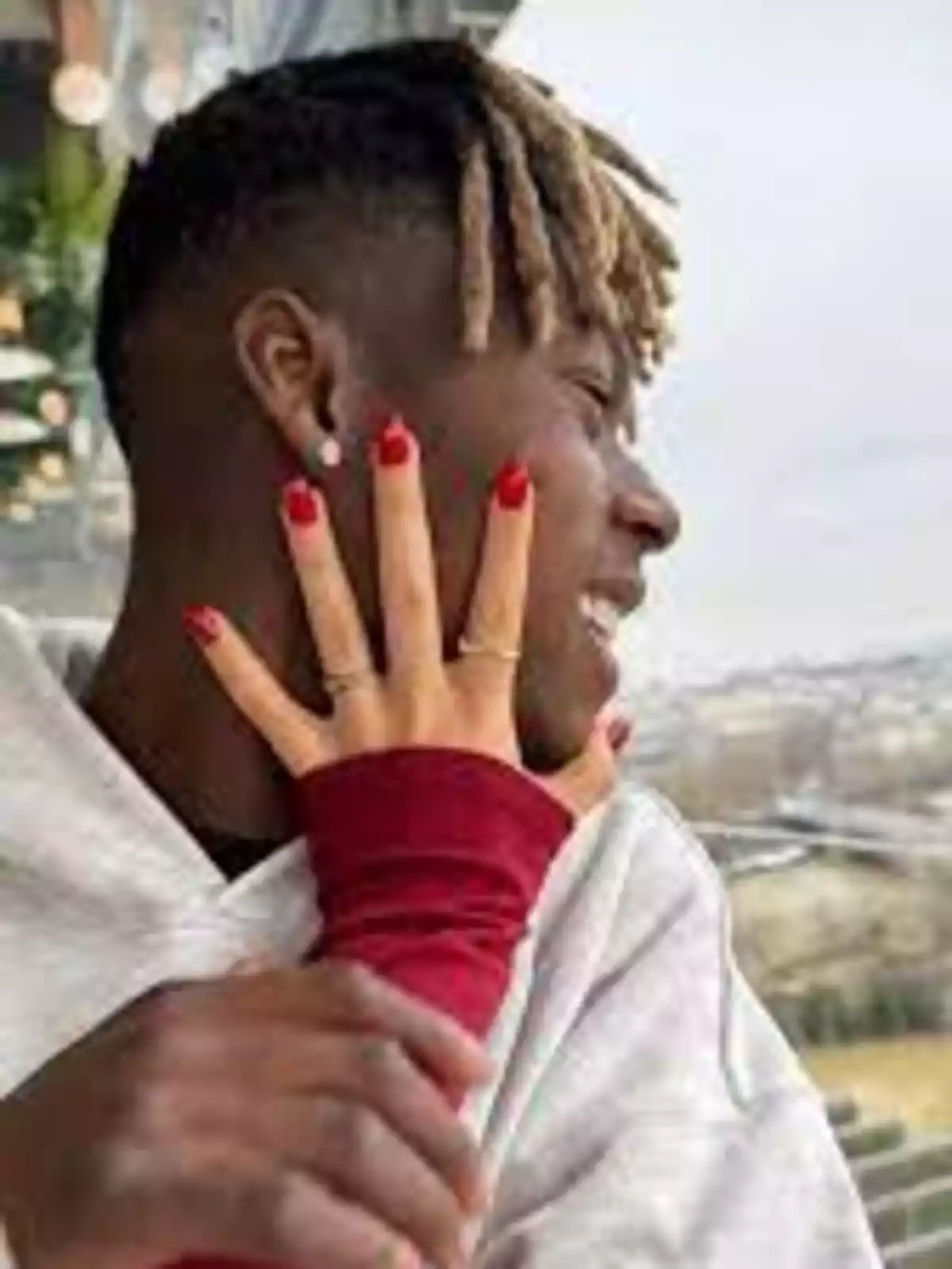 Un hombre sonriente con el rostro cubierto parcialmente por la mano de una mujer con uñas rojas y anillos Un hombre sonriente con el rostro cubierto parcialmente por la mano de una mujer con uñas rojas y anillos