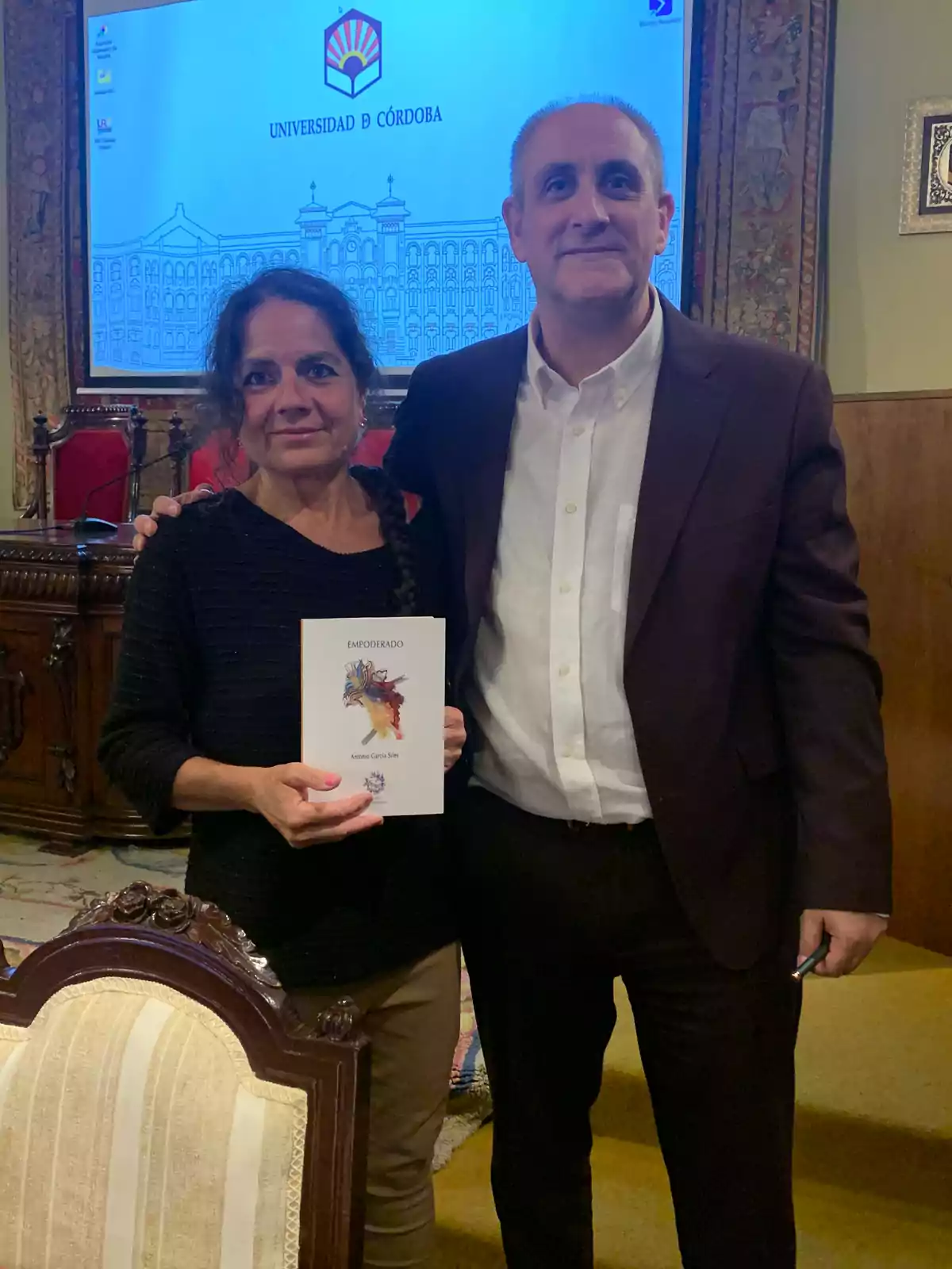 una mujer vestida de negro sujeta un libro junto a un hombre vestido de traje una mujer vestida de negro sujeta un libro junto a un hombre vestido de traje