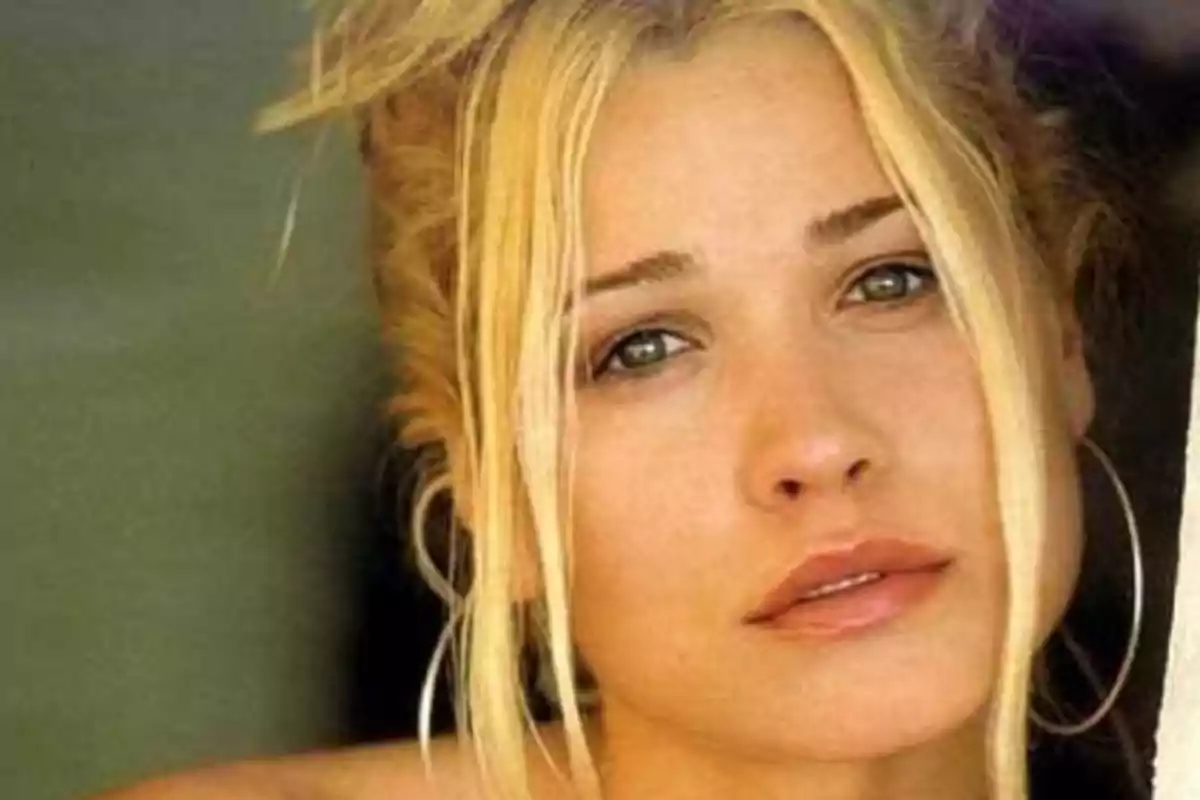 Mujer rubia de cabello recogido con mechones sueltos y expresión seria mirando a la cámara