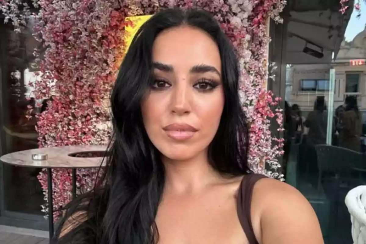 Mujer de cabello largo y oscuro posando frente a una pared decorada con flores rosas y blancas