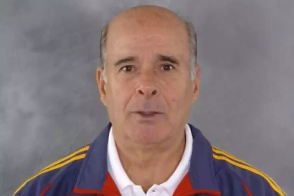 Hombre mayor calvo con chaqueta deportiva azul con detalles amarillos y fondo gris Hombre mayor calvo con chaqueta deportiva azul con detalles amarillos y fondo gris