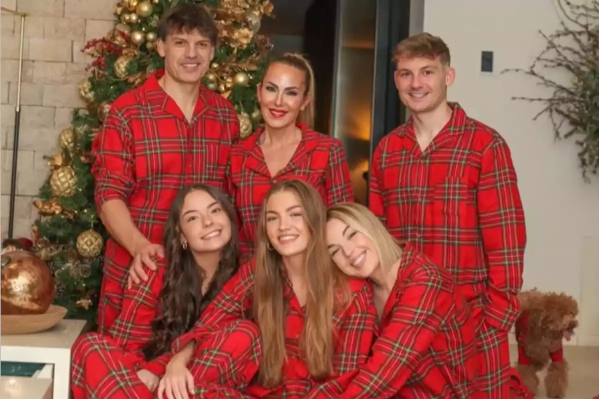 Familia posando frente a un árbol de Navidad, todos usando pijamas rojas a cuadros y un perro pequeño también con pijama similar