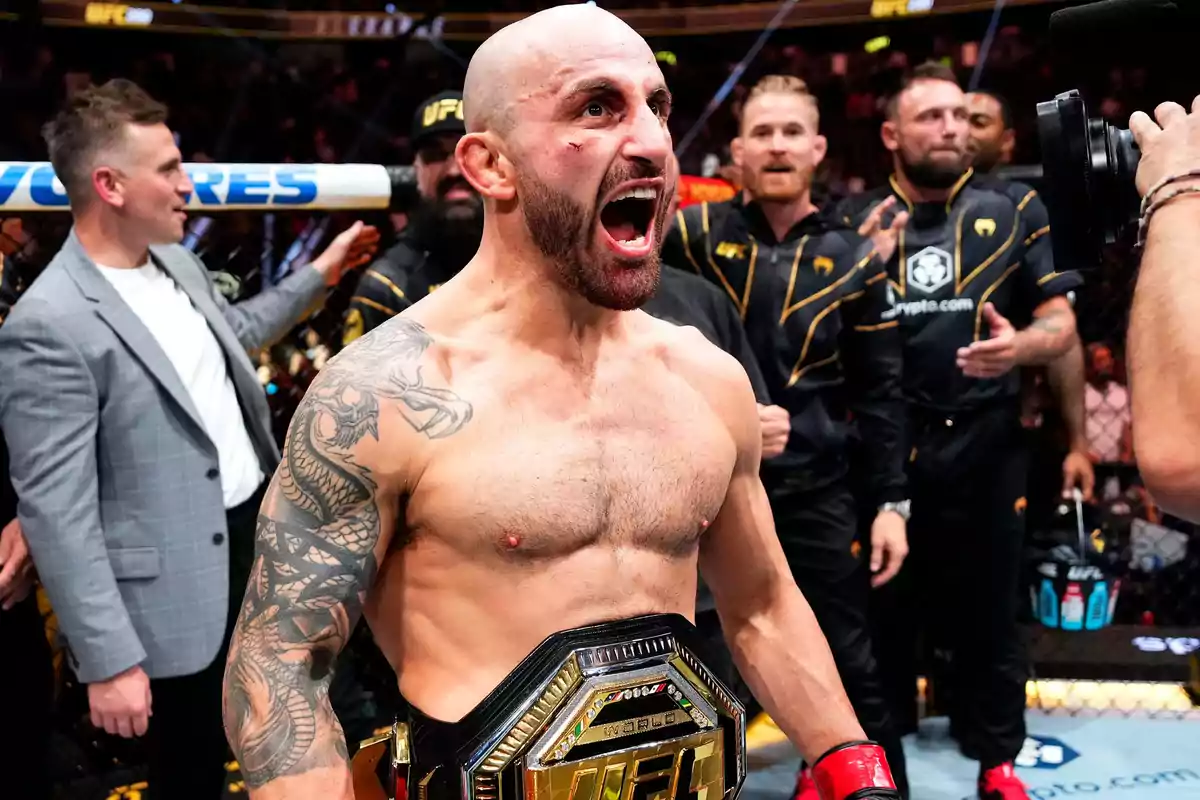 Un luchador de artes marciales mixtas celebra con el cinturón de campeón en el octágono rodeado de su equipo y aficionados Un luchador de artes marciales mixtas celebra con el cinturón de campeón en el octágono rodeado de su equipo y aficionados