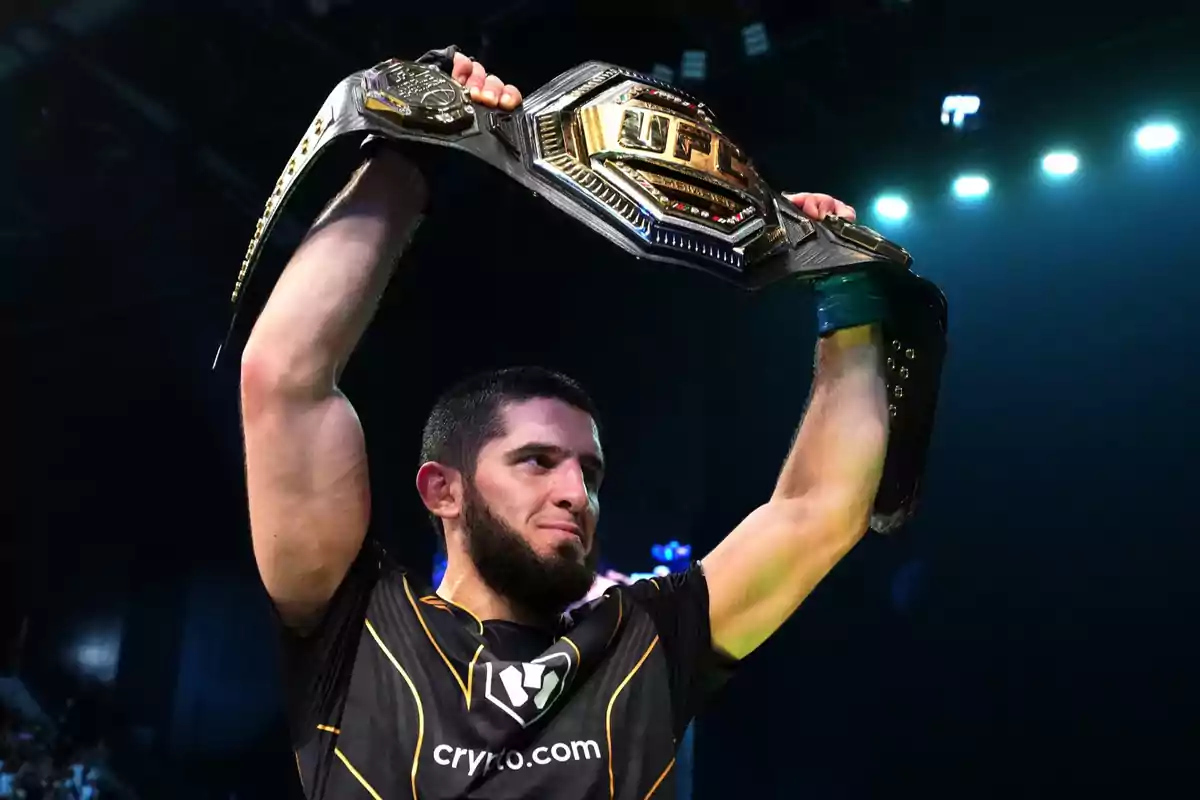Un luchador de artes marciales mixtas sostiene un cinturón de campeón de la UFC sobre su cabeza en señal de victoria Un luchador de artes marciales mixtas sostiene un cinturón de campeón de la UFC sobre su cabeza en señal de victoria