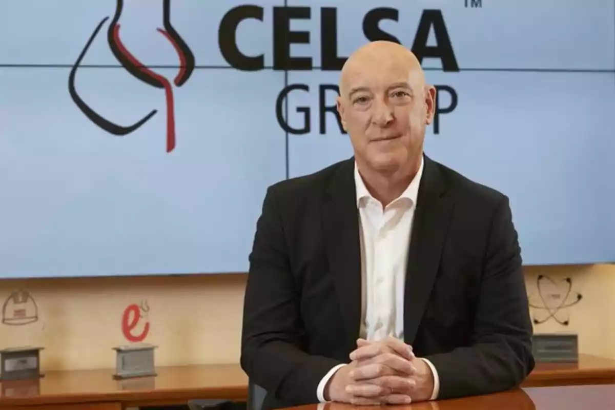 Hombre calvo con traje oscuro y camisa blanca sentado en una mesa frente a un fondo con el logo de Celsa Group