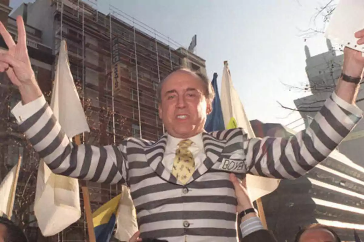Hombre con traje a rayas blancas y negras levantando los brazos en señal de victoria en una manifestación al aire libre con banderas y edificios de fondo Hombre con traje a rayas blancas y negras levantando los brazos en señal de victoria en una manifestación al aire libre con banderas y edificios de fondo