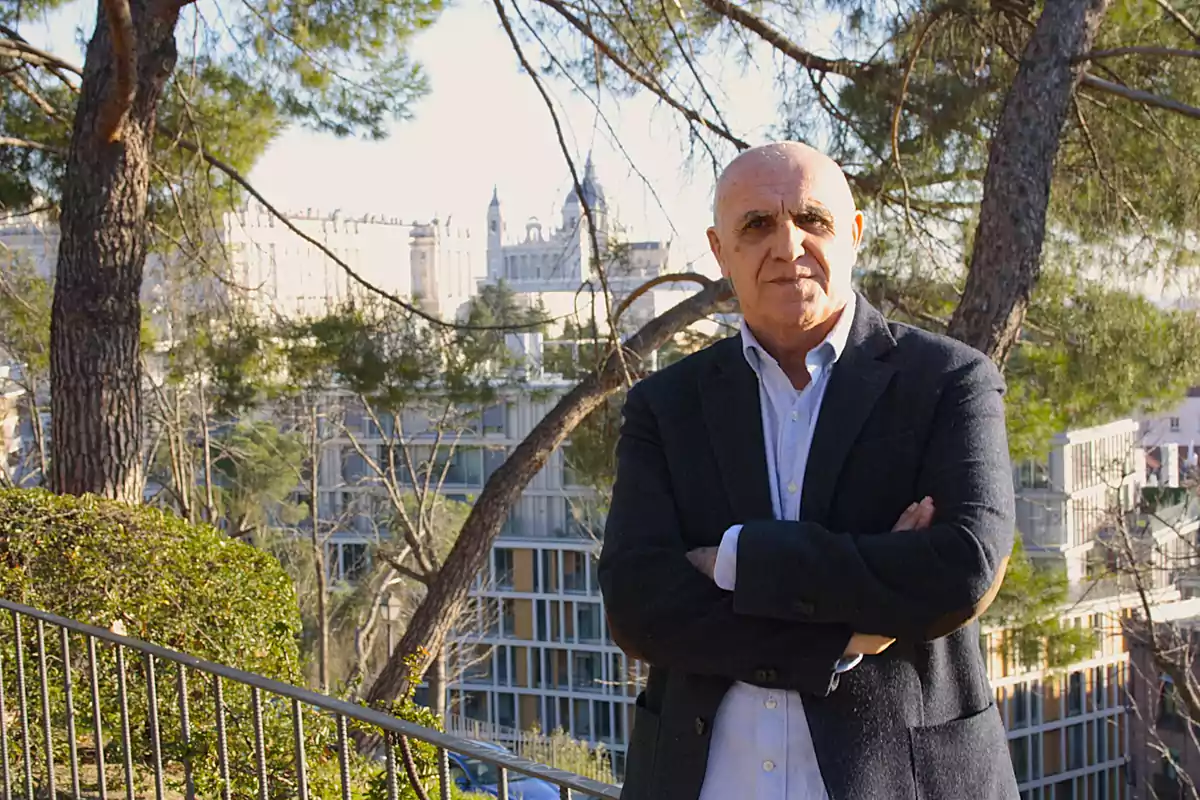 Hombre de cabello corto y canoso con chaqueta oscura y camisa clara posando con los brazos cruzados en un entorno urbano con árboles y edificios al fondo Hombre de cabello corto y canoso con chaqueta oscura y camisa clara posando con los brazos cruzados en un entorno urbano con árboles y edificios al fondo