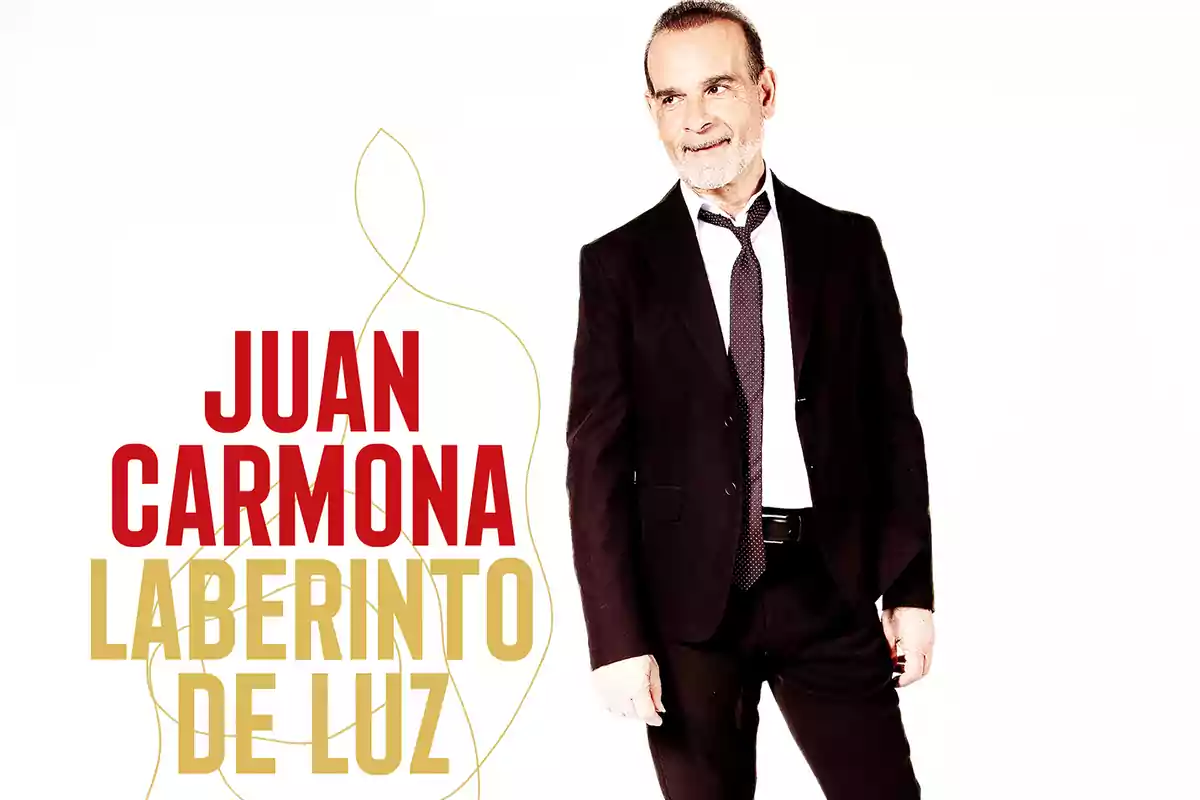 Hombre de traje oscuro con camisa blanca y corbata, de pie junto a un fondo blanco con el texto Juan Carmona Laberinto de Luz en letras grandes