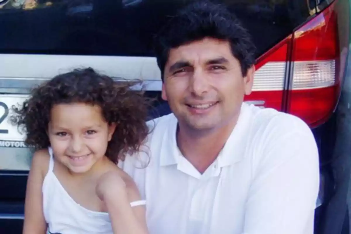 Hombre y niña sonríen juntos frente a un auto negro Hombre y niña sonríen juntos frente a un auto negro