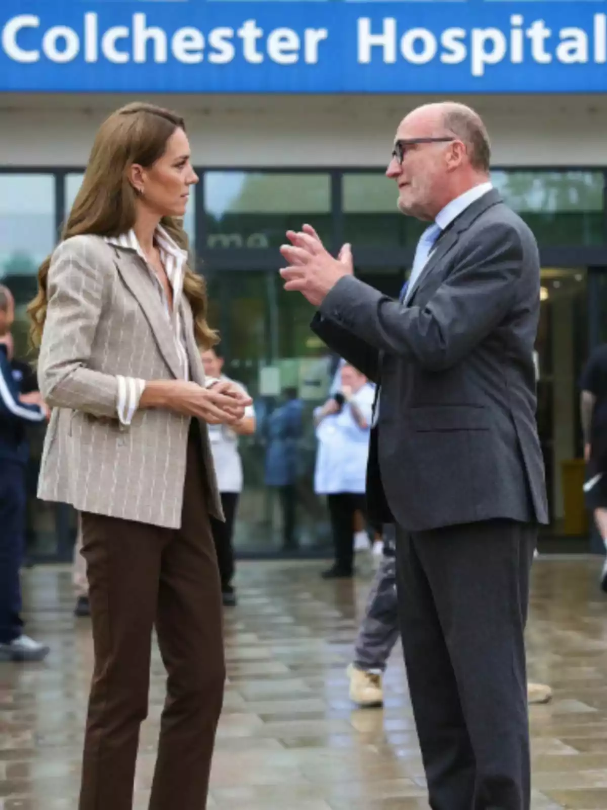 Kate Middleton and a man are talking in front of the entrance to a hospital called Colchester Hospital. Kate Middleton and a man are talking in front of the entrance to a hospital called Colchester Hospital.