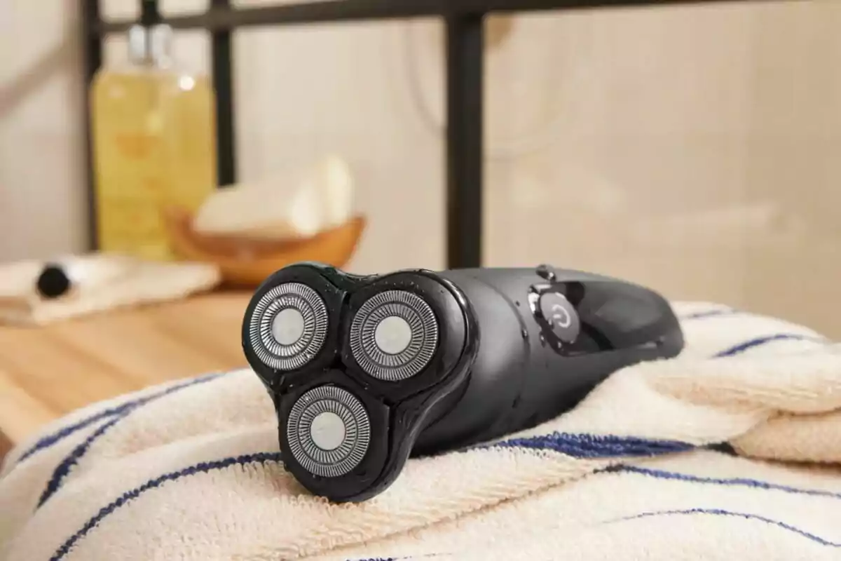 Rasuradora eléctrica negra con cabezales circulares sobre una toalla blanca con rayas azules en un baño Rasuradora eléctrica negra con cabezales circulares sobre una toalla blanca con rayas azules en un baño