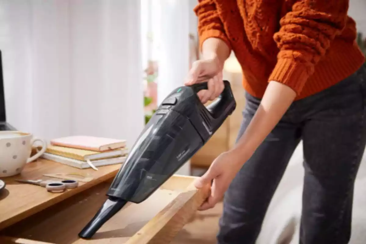 Persona usando una aspiradora de mano para limpiar el interior de un cajón de madera en un escritorio Persona usando una aspiradora de mano para limpiar el interior de un cajón de madera en un escritorio