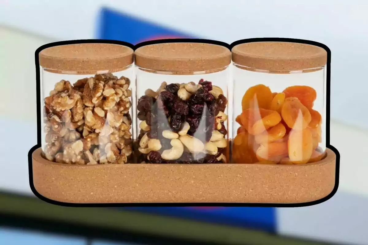 Tres frascos de vidrio con tapa de corcho contienen nueces, mezcla de frutos secos y orejones de durazno, todos colocados en una bandeja de corcho. Tres frascos de vidrio con tapa de corcho contienen nueces, mezcla de frutos secos y orejones de durazno, todos colocados en una bandeja de corcho.