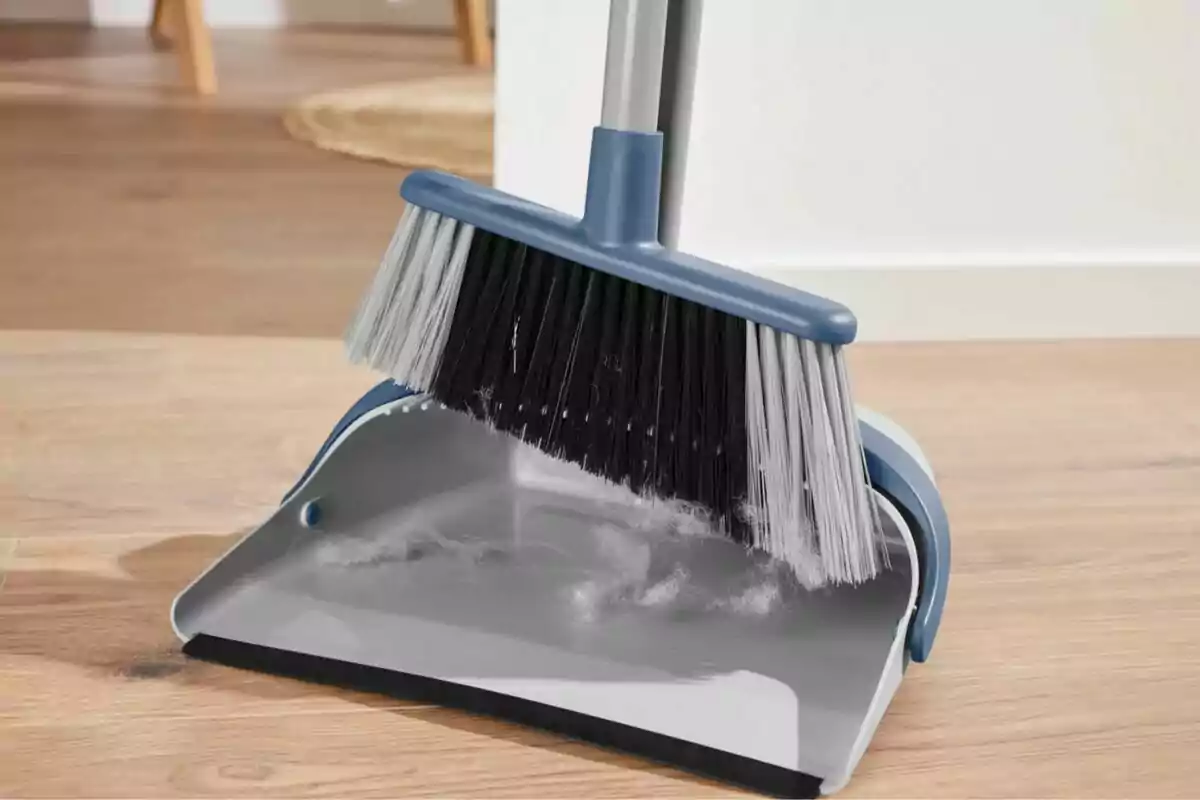 Escoba y recogedor azul con polvo y pelusa sobre un piso de madera Escoba y recogedor azul con polvo y pelusa sobre un piso de madera