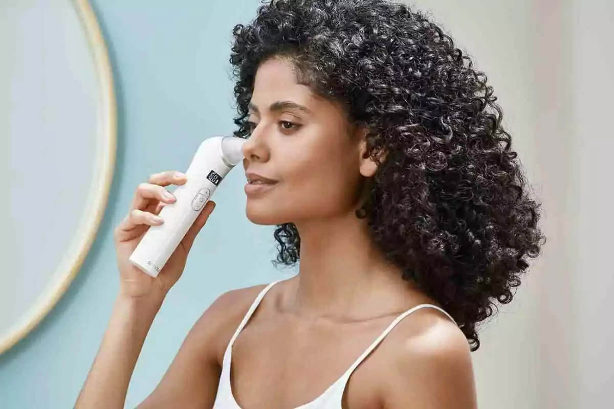 Mujer de cabello rizado usando un dispositivo de limpieza facial eléctrico en la nariz Mujer de cabello rizado usando un dispositivo de limpieza facial eléctrico en la nariz