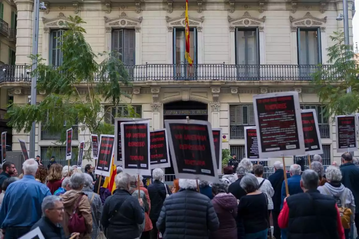 Un grupo de personas se manifiesta frente a un edificio oficial sosteniendo carteles con mensajes de protesta Un grupo de personas se manifiesta frente a un edificio oficial sosteniendo carteles con mensajes de protesta