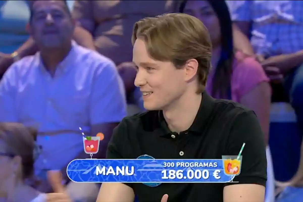 Un joven con camisa negra sonríe mientras participa en un concurso televisivo, con un rótulo que muestra su nombre, la cantidad de programas y el dinero acumulado, rodeado de público en el fondo. Un joven con camisa negra sonríe mientras participa en un concurso televisivo, con un rótulo que muestra su nombre, la cantidad de programas y el dinero acumulado, rodeado de público en el fondo.