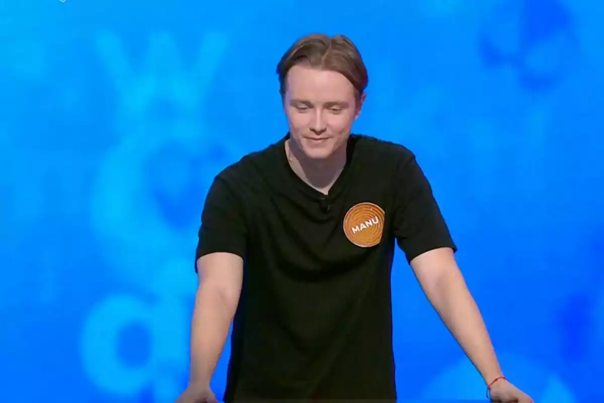 Manu Pascual con camiseta negra y una etiqueta que dice Manu participando en un concurso televisivo con fondo azul. Manu Pascual con camiseta negra y una etiqueta que dice Manu participando en un concurso televisivo con fondo azul.