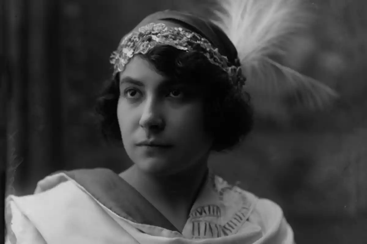 Retrato en blanco y negro de una mujer joven con cabello corto y ondulado que lleva una diadema decorada con pedrería y una pluma grande Retrato en blanco y negro de una mujer joven con cabello corto y ondulado que lleva una diadema decorada con pedrería y una pluma grande