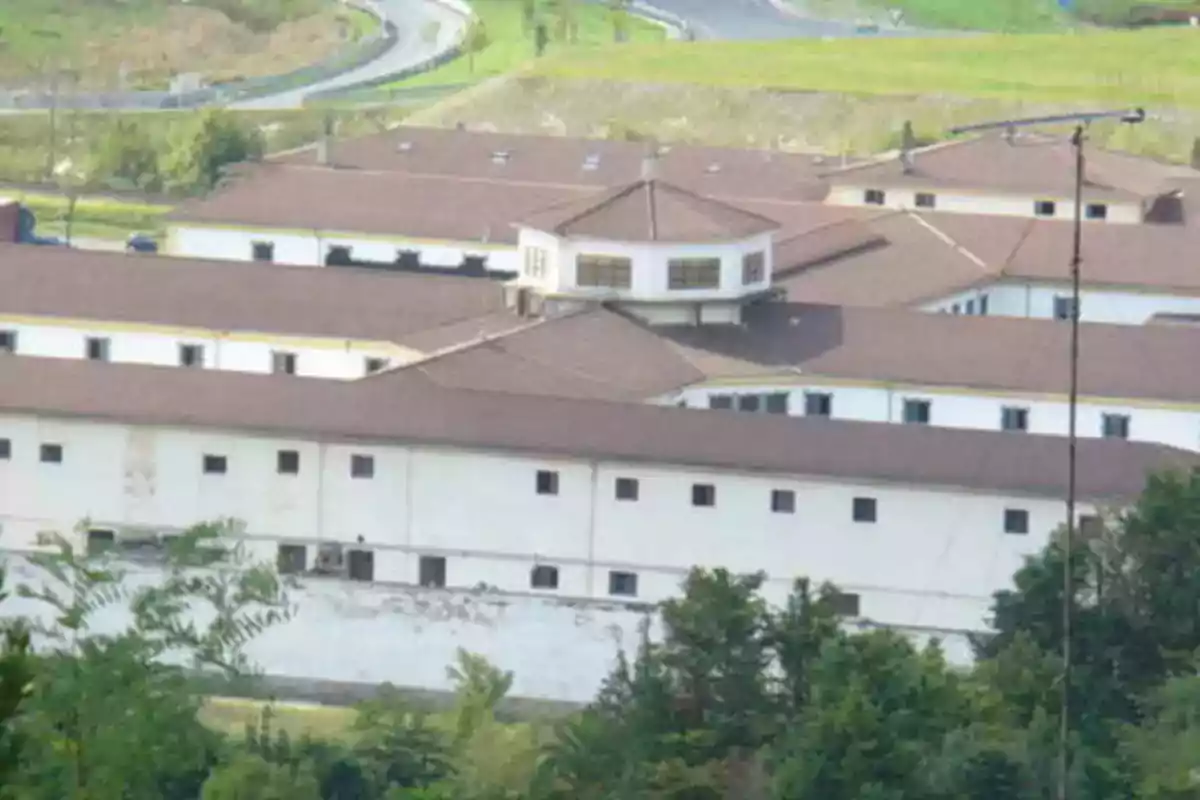Edificio grande de paredes blancas y techo marrón rodeado de vegetación y caminos asfaltados Edificio grande de paredes blancas y techo marrón rodeado de vegetación y caminos asfaltados