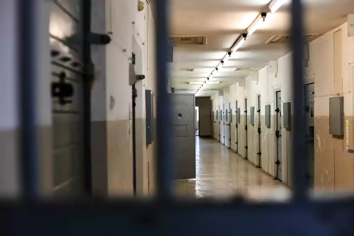 Pasillo de una prisión con varias puertas de celdas metálicas y luz fluorescente