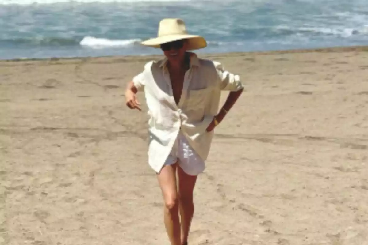 Meghan Markle wearing a big hat and sunglasses walking on the beach with the sea in the background. Meghan Markle wearing a big hat and sunglasses walking on the beach with the sea in the background.