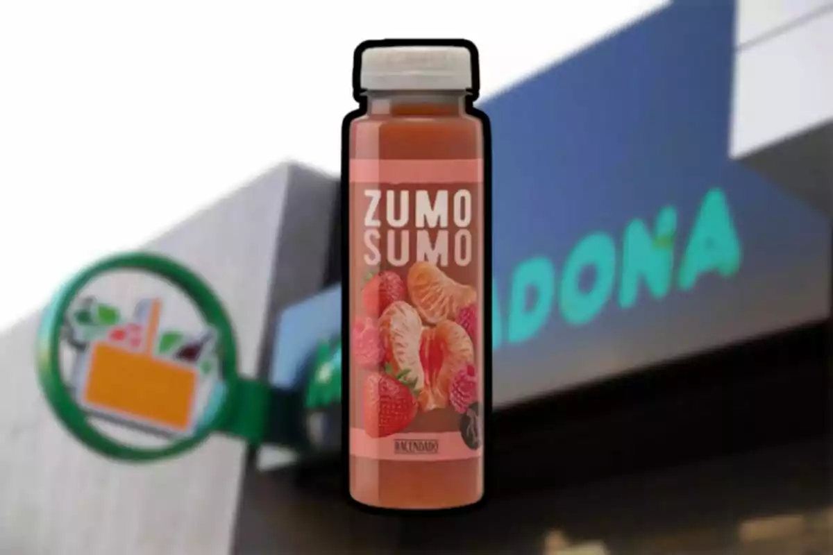 Botella de zumo de fresa y mandarina de la marca Hacendado frente a una tienda Mercadona desenfocada Botella de zumo de fresa y mandarina de la marca Hacendado frente a una tienda Mercadona desenfocada