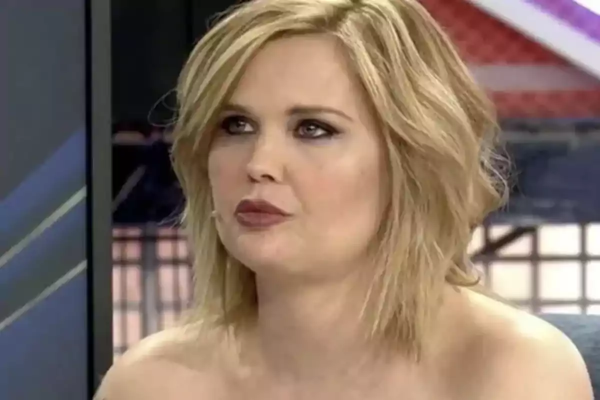 Mujer rubia de cabello corto y maquillaje marcado sentada en un estudio de televisión
