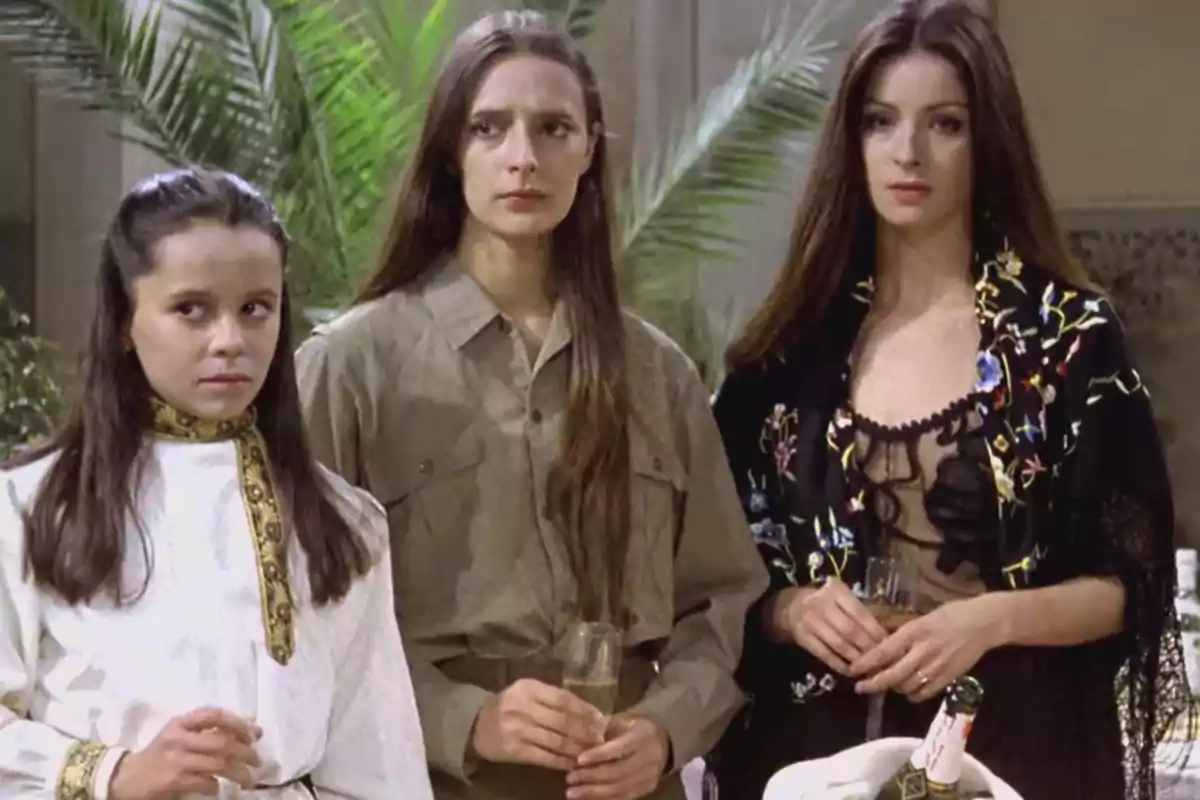 Tres mujeres jóvenes con cabello largo y suelto están de pie juntas en un ambiente elegante, cada una sosteniendo una copa, con expresiones serias y vestidas con ropa de diferentes estilos Tres mujeres jóvenes con cabello largo y suelto están de pie juntas en un ambiente elegante, cada una sosteniendo una copa, con expresiones serias y vestidas con ropa de diferentes estilos