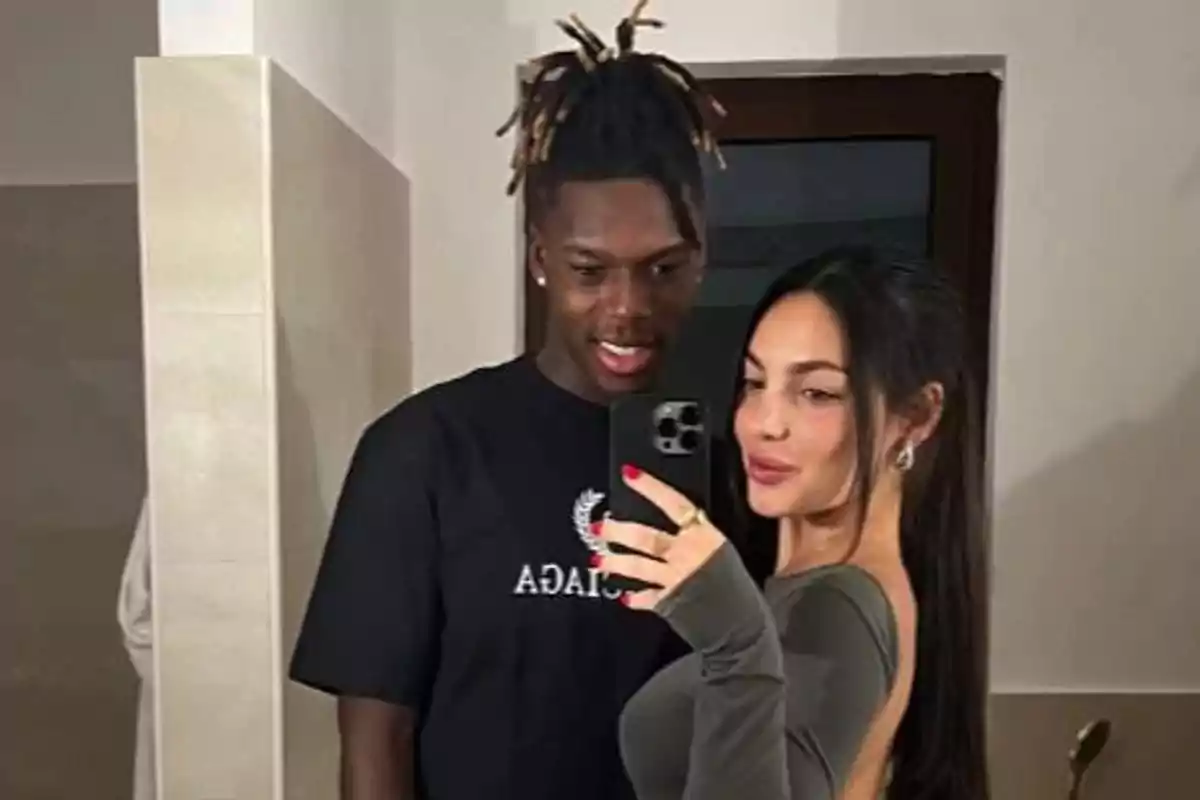 Una pareja joven se toma una selfie frente a un espejo en un baño, ambos sonríen y la mujer sostiene el teléfono móvil Una pareja joven se toma una selfie frente a un espejo en un baño, ambos sonríen y la mujer sostiene el teléfono móvil