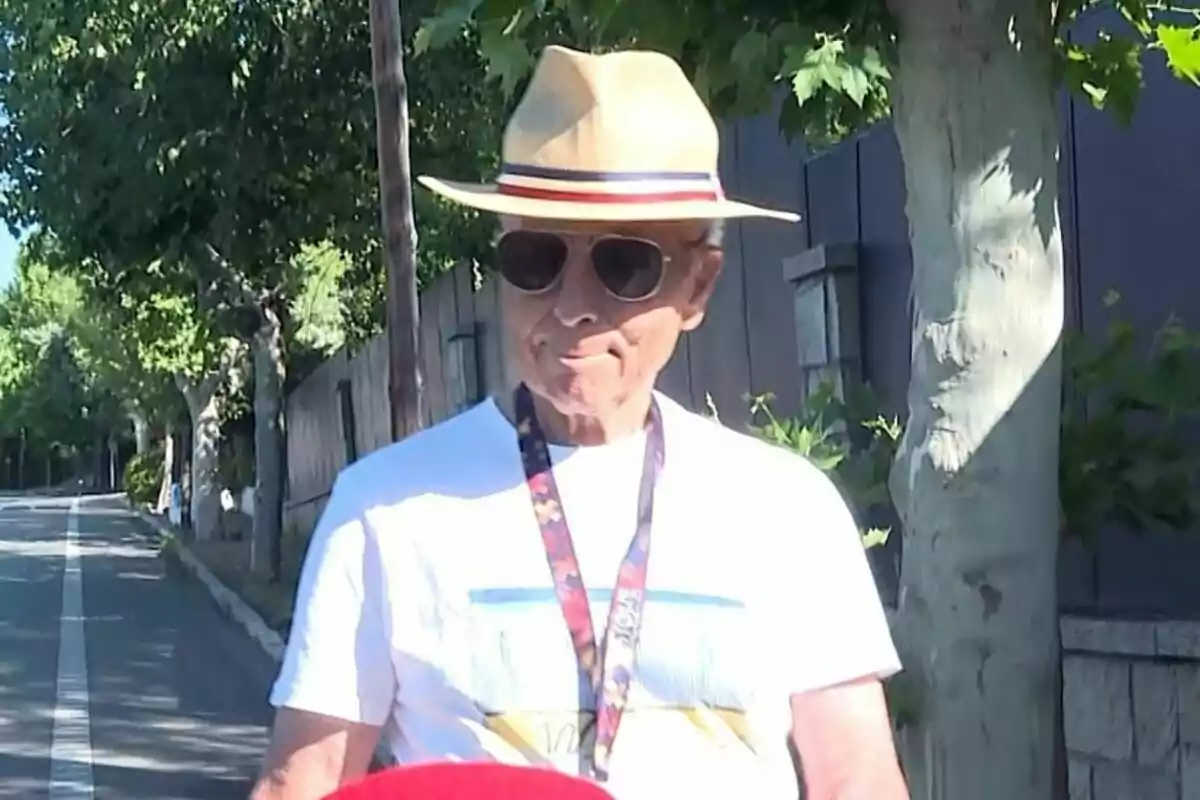 Plano medio de José Ortega Cano con sombrero de ala ancha y gafas de sol caminando por una calle arbolada en un día soleado. Plano medio de José Ortega Cano con sombrero de ala ancha y gafas de sol caminando por una calle arbolada en un día soleado.