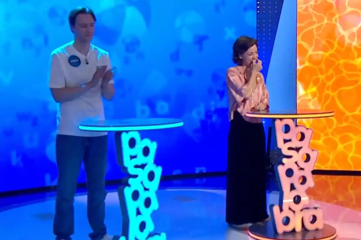 Manu y Rosa participan en un programa de televisión de preguntas y respuestas, uno aplaude mientras la otra sonríe emocionada junto a sus atriles iluminados. Captura de 'Pasapalabra' Manu y Rosa participan en un programa de televisión de preguntas y respuestas, uno aplaude mientras la otra sonríe emocionada junto a sus atriles iluminados. Captura de 'Pasapalabra'