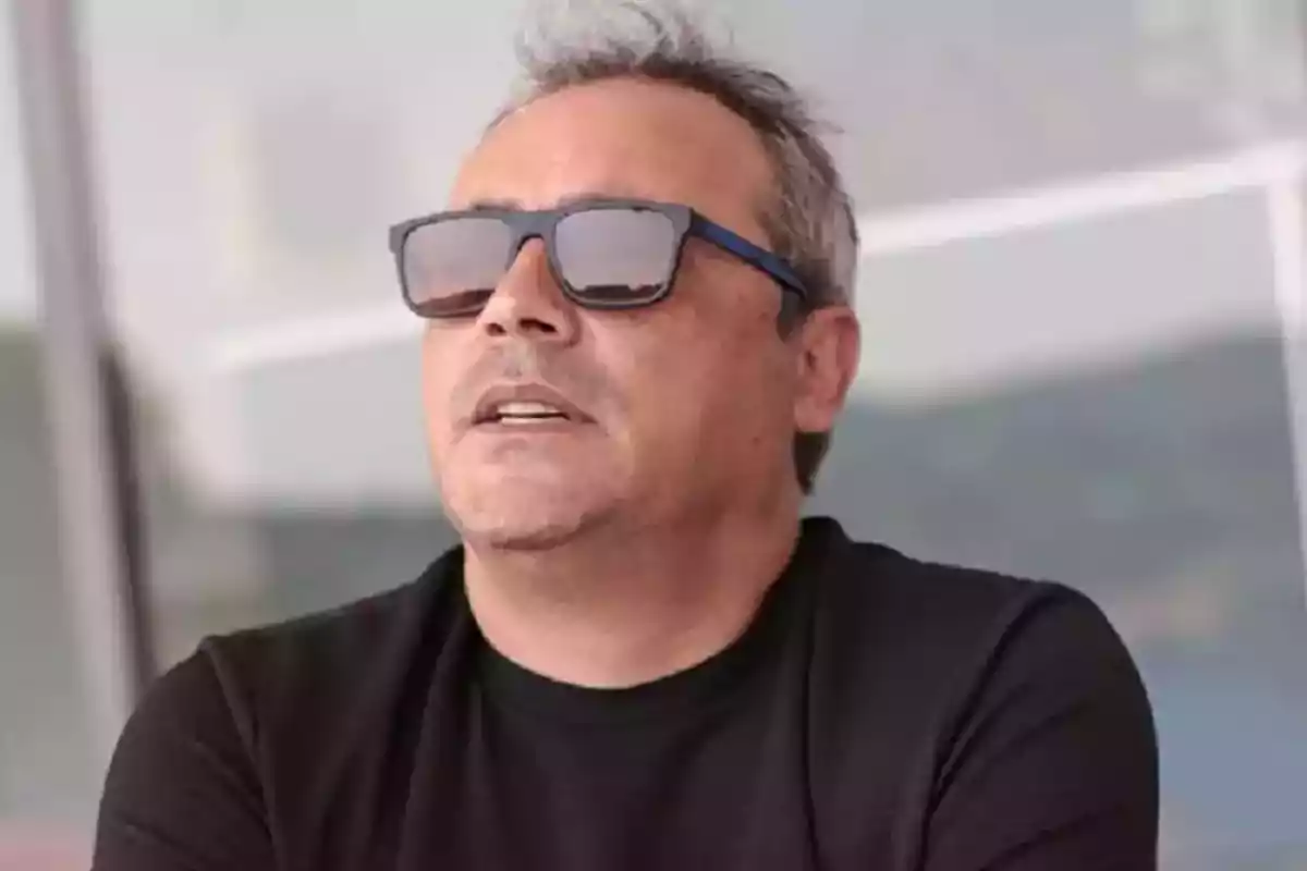 Hombre de cabello corto y canoso usando gafas de sol y camiseta negra en un entorno al aire libre Hombre de cabello corto y canoso usando gafas de sol y camiseta negra en un entorno al aire libre